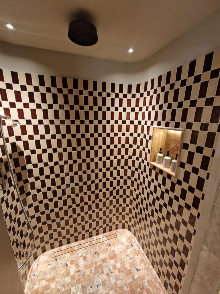 Curved corner shower with mosaic tile in hotel bathroom, formed using offsite radiused corner cassettes