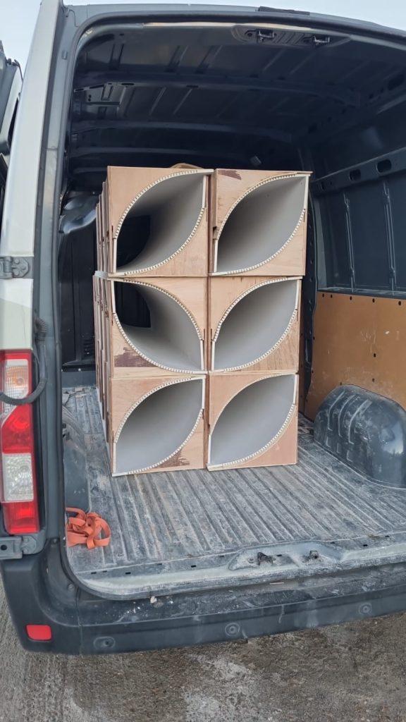 Offsite-fabricated radiused corner cassettes with petal-shaped curved cutouts, loaded in a van ready for delivery to site