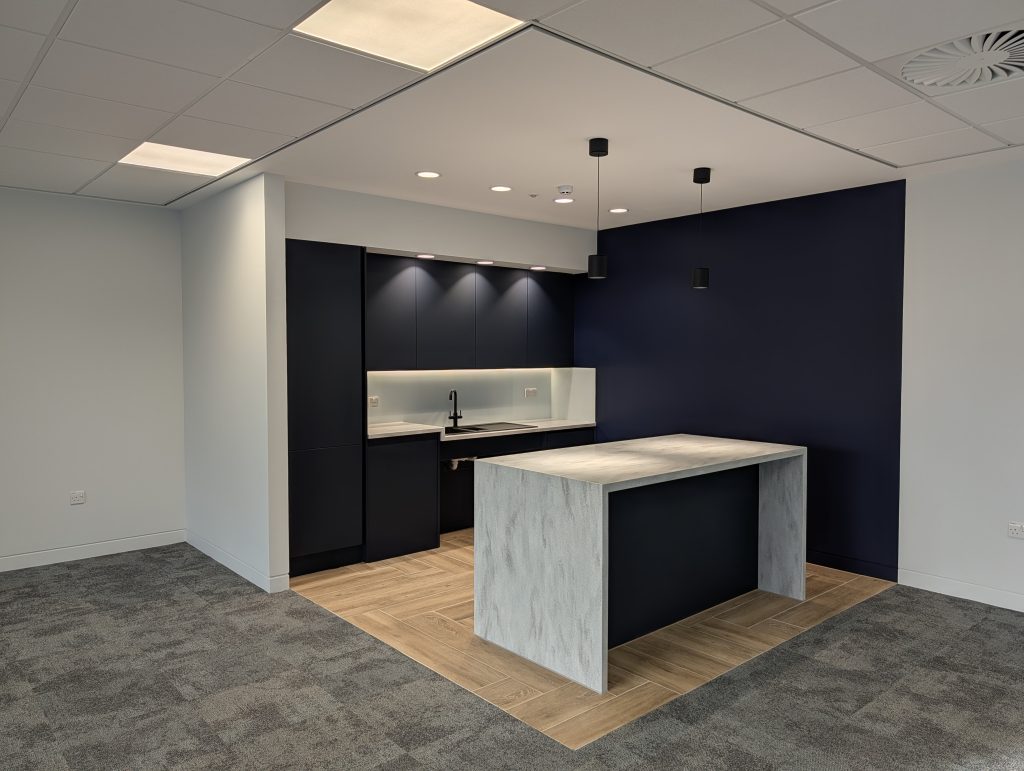 Shadow gap skirting in a modern office kitchenette fit-out with navy units and wood-effect flooring